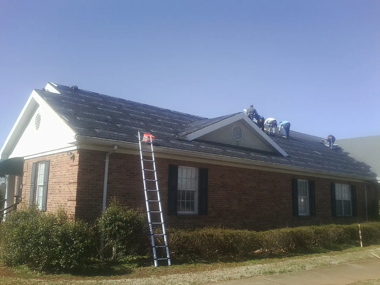 Crew tearing shingles off a brick ranch roof with a ladder set — Emergency Roof Repair work by our crew in Chimacum