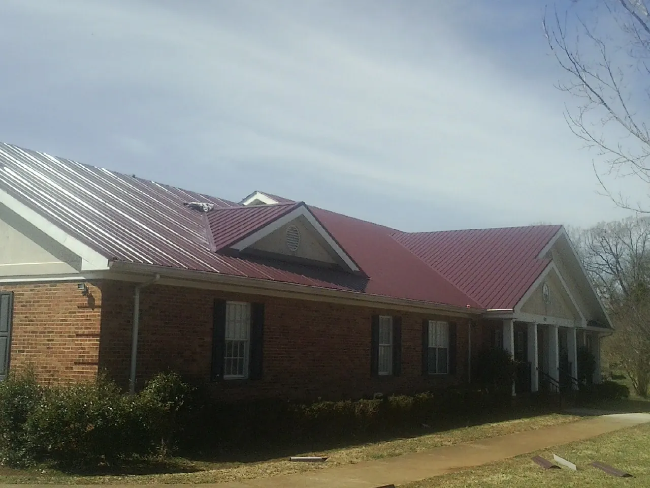 Red metal roof with gabled entries on a long brick building, from a Hail Damage Roof Repair job in Chimacum