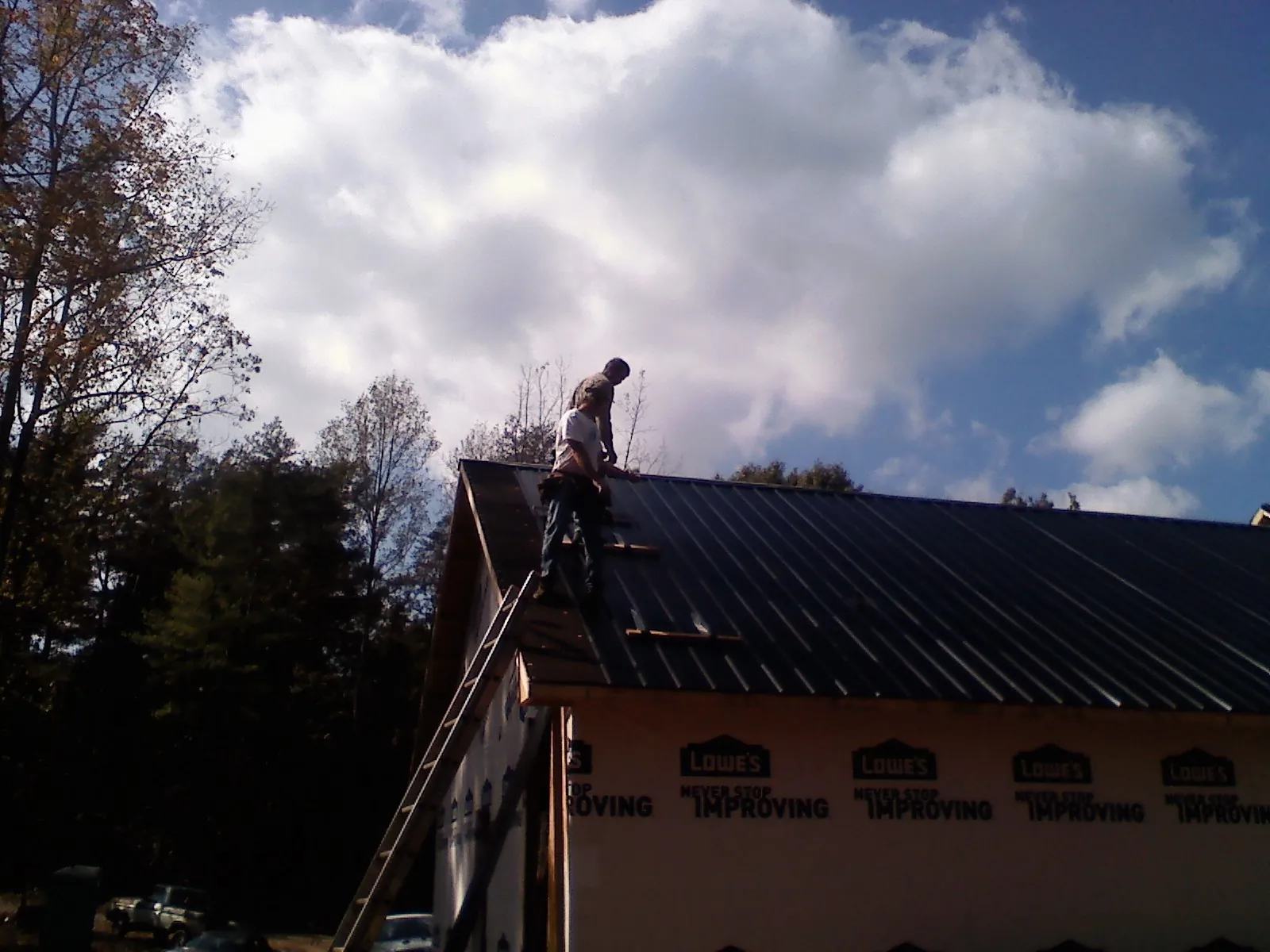 Roofer fastening dark metal panels high against a cloudy sky, from a Roof Inspection job in Chimacum
