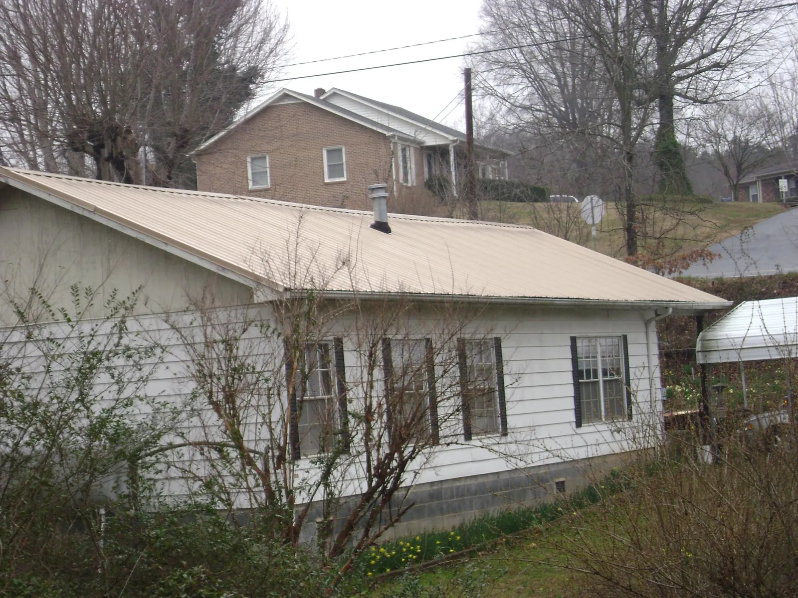 Tan metal roof on a white sided house set into a hillside — Commercial Roofing by Roofing Brothers in Chimacum